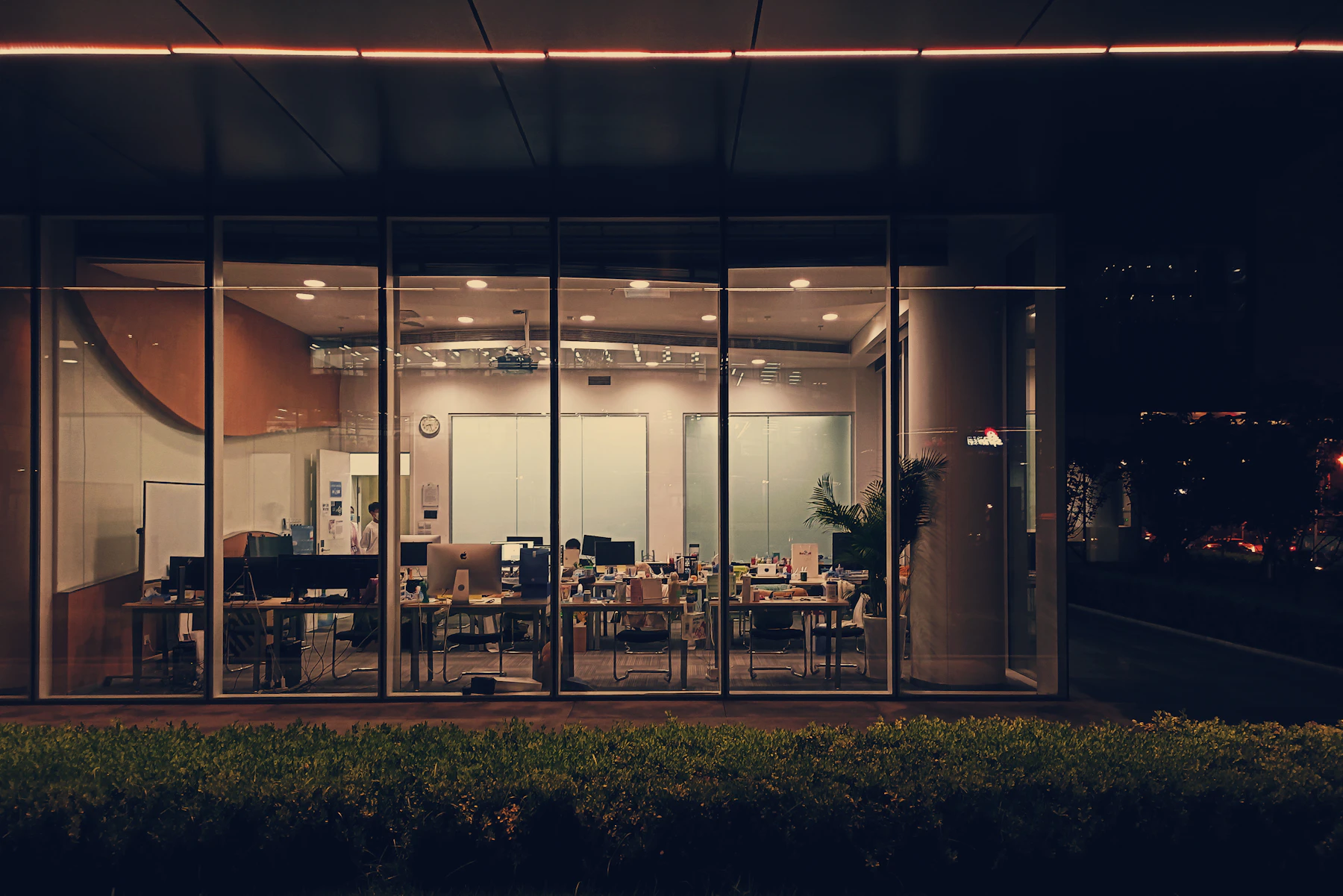 An office still lit behind its window wall long after dark