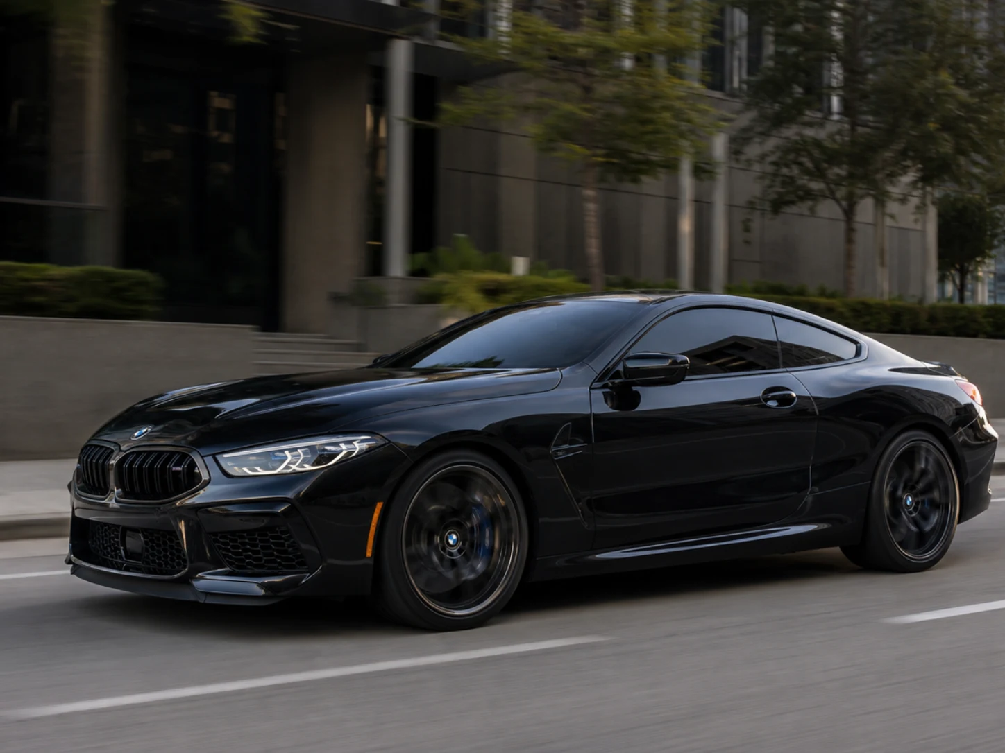 A black BMW M8 with dark tinted windows driving through a modern city